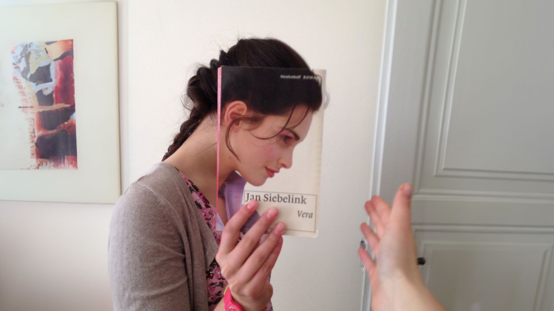 Een vrouw houdt een boek voor haar gezicht, op de cover staat een vrouwengezicht afgebeeld - ter illustratie bij blog uitgeverij haystack